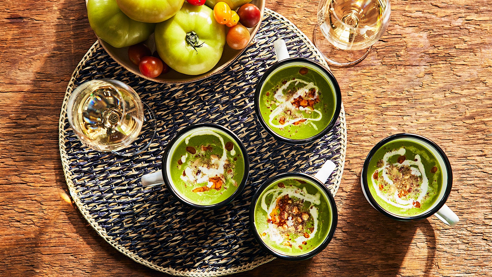 Four mugs of green gazpacho, two glasses of white wine and a bowl of tomatoes